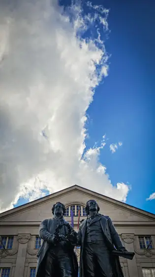 Esculturas frente a un edificio de composición clásica.