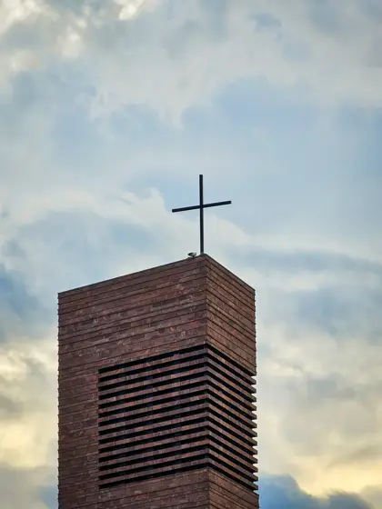 Campanario de ladrillo: lamas horizontales y una cruz en el cielo.