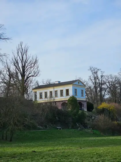 Casa blanca elevada sobre un jardín arbolado.